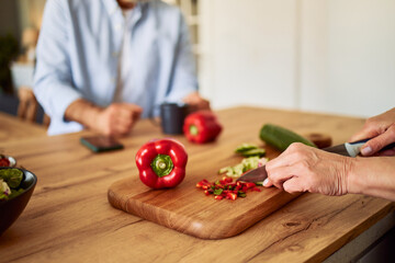 A close-up shot of adult female hands cutting vegetables into small pieces on a wooden cutting board and preparing a salad