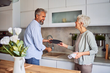 A loving senior couple smiling at each other and doing the dishes together in the kitchen