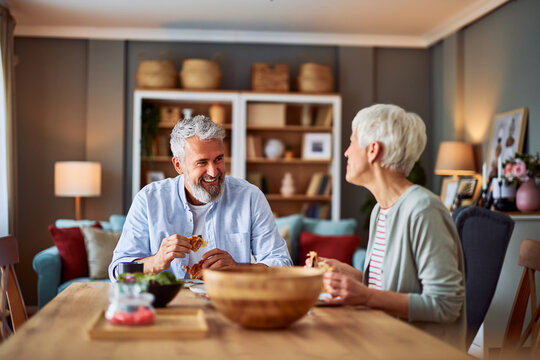 A joyful old married couple laughing and enjoying breakfast together at the dining table