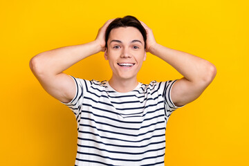 Portrait of impressed guy with brunet hair wear stylish t-shirt keep arms on head staring at discount isolated on yellow color background