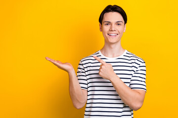 Portrait of optimistic handsome student wear stylish t-shirt indicating at offer on palm empty...