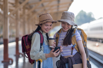 two young asian friends girls with backpacks at railway station waiting for train, Two beautiful...