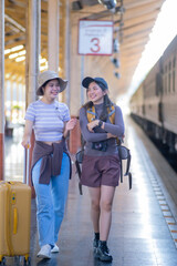 two young asian friends girls with backpacks at railway station waiting for train, Two beautiful women walking along platform at train station