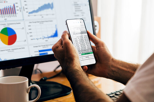 Man using Sheets app on a mobile phone and laptop. Google Workspace, online digital productivity tools. Using spreadsheet.