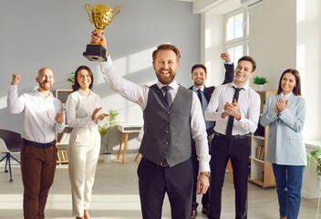 Happy winner businessman receives a business award. Joyful man holding his trophy, with a team of cheerful workers in the background celebrating and congratulating their leader on great work success - obrazy, fototapety, plakaty