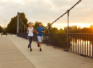 Sporty happy smiling couple in sportswear jogging along a bridge in the park having sport workout....