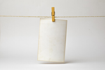 An empty, aged photo paper note is suspended from a twine using wooden clothespins against a...