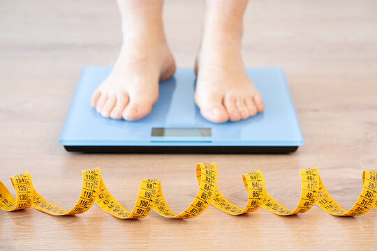 Tape measure and woman feet standing on weigh scales.Diet,weight loss and feet of a woman on a scale for body check,measure and balance to lose weight on the floor. Obesity,scales and girl with tape