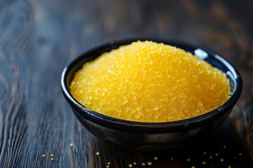 A bowl, filled with yellow sugar, sits on a dark wood table, its rounded shape and exotic look are emphasized by the stipple effect.