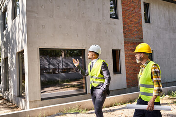 commited architect and builder in safety vests holding blueprint and discussing construction process
