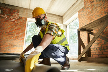 hardworking construction worker in safety helmet and gloves with dust mask putting carpet on floor - 742713288