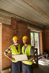 hardworking construction workers in safety vests working with laptop on site, cottage builders