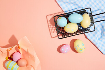 View from above with black basket of colorful Easter eggs decorated with blue checkered on pink background. Empty space for design