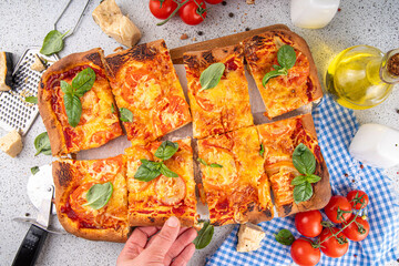Rectangular homemade margarita pizza with tomatoes and basil, with ingredients and olive oil on white kitchen table background