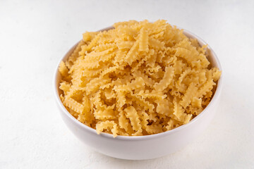 Raw uncooked Mafaldine pasta with ingredients for cooking. Short italian Mafaldine pasta with olive oil, cherry tomatoes, basil, spices on white kitchen table, background copy space