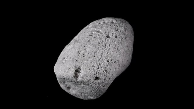 Pumice (volcanic rock) specimen rotating slowly against a black background.	
