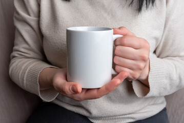 Hands of a woman hold a white clean mug, presenting a spotless surface for promoting unique mug...