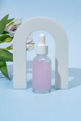 Beauty Collagen face serum in a glass dropper bottle Arch on blue background with alstromeria flower. Trendy shoot of cosmetics packaging Essential oil with natural ingredients Copy Space