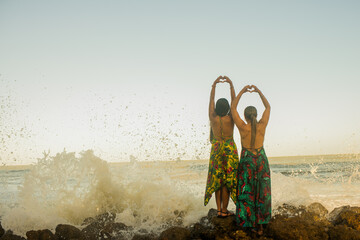 pareja de espaldas frente al mar haciendo corazón con sus manos  - obrazy, fototapety, plakaty
