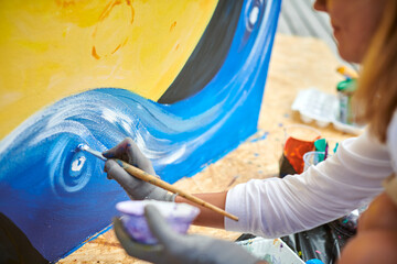 Female painter in black cap draws picture with paintbrush on canvas for outdoor street exhibition,...