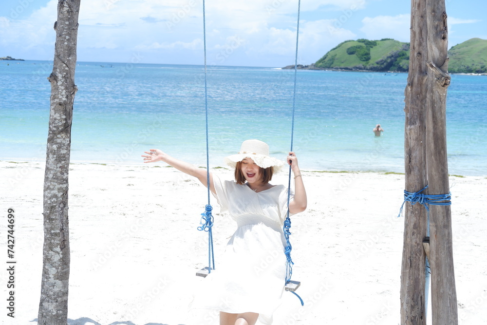 Wall mural woman in white dress and hat swinging on tropical beach, sunny day, good weather on lombok beach