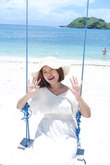 Woman in white dress and hat swinging on tropical beach, sunny day, good weather on lombok beach