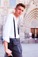 Young European guy in shirt and trousers with suspenders walking around city