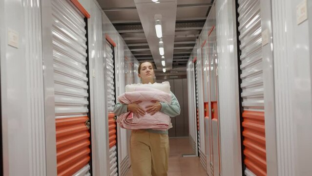 Woman with her stuff enters in the self-storage facility unit. White and orange closed metal doors of storage warehouse. Moving, organizing, storage concept.