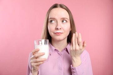 Cute woman with milk mustache holding glass of tasty dairy drink on pink background
