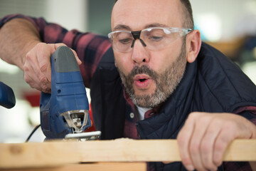 man using jigsaw blowing sawdust from wood