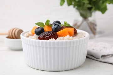 Delicious barley porridge with blueberries, pumpkin, dates and mint in bowl on white table, closeup