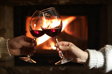 Couple clinking glasses of wine near fireplace at home, closeup