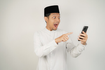 Wow face of Asian Muslim man shocked what he see in the smartphone on isolated background