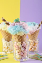 Sweet cotton candies in waffle cones and marshmallows on color background, closeup