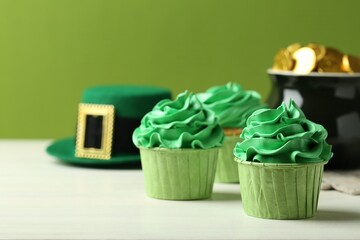 St. Patrick's day party. Tasty cupcakes with green cream, pot of gold and leprechaun hat on white...