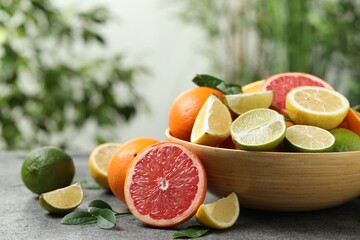 Different fresh citrus fruits and leaves on table against blurred background, closeup