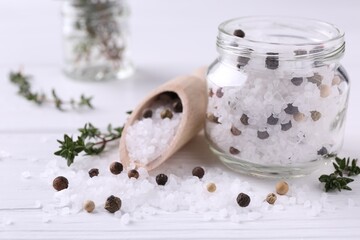 Fototapeta na wymiar Salt with peppercorns in glass jar, thyme and scoop on white wooden table, closeup