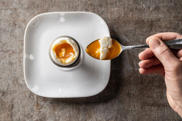 A woman's hand with a spoon scoops a soft-boiled egg from the shell - Top of view - 742778638