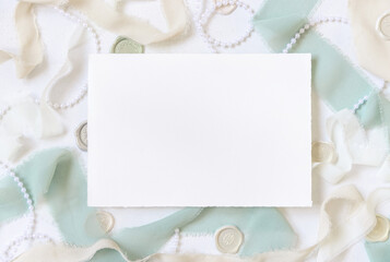 Card near light green and beige silk ribbons and decorations on white table top view, mockup