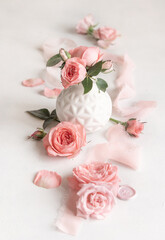 Light pink roses in a vase, petals and buds on white table close up, romantic and wedding