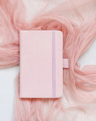 Pink hardcover notebook on tulle fabric on white table top view, textbook mockup
