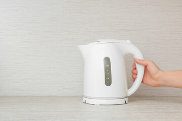 Young adult woman hand holding white plastic electric kettle on stone table top at home kitchen....