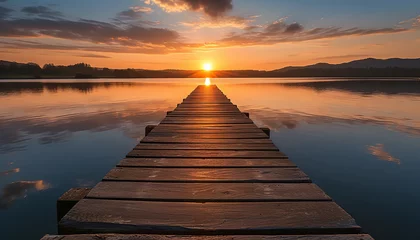 Fotobehang A tranquil scene captures a wooden jetty reaching out into calm waters - with the glow of sunset reflecting off the surface - wide format © Davivd