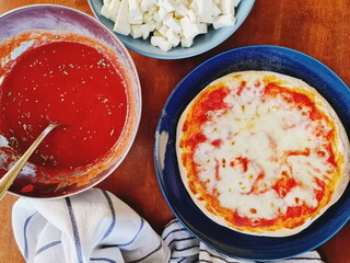 pizza on a blue plate with tomato sauce and mozzarella in two bowls