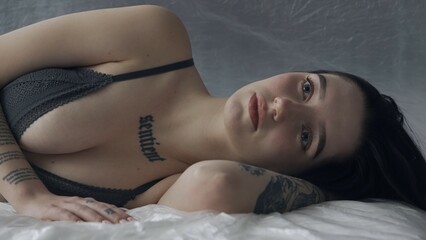 Female in underwear laying on the bed in the studio. Young woman seminude in lingerie laying posing...
