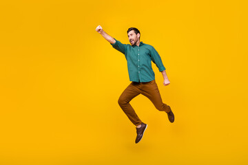 Full size photo of brave guy dressed dotted shirt brown trousers fly in empty space raising fist up isolated on yellow color background