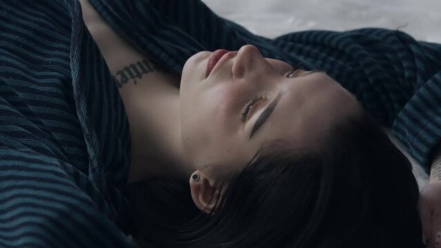 Female in sleepwear laying on the bed in the studio. Young woman in pajama shirt laying posing under thin sheet of oilcloth wrap.