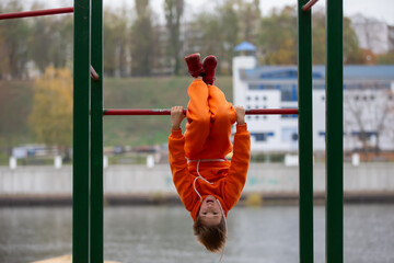 A teenage boy is engaged on horizontal bars, doing exercises and hanging upside down.
