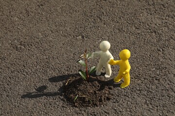 Human figures with soil and green seedling on asphalt road