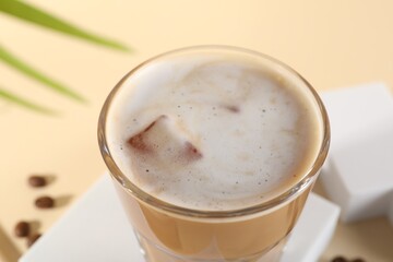Refreshing iced coffee with milk in glass on pale yellow table, closeup